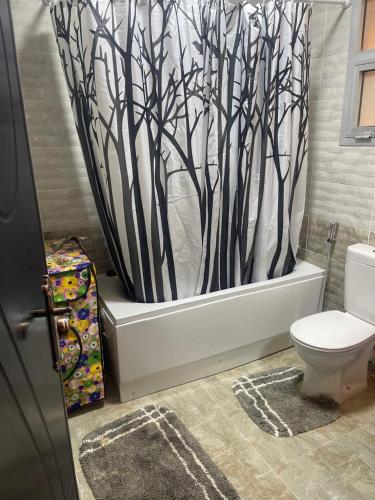 a bathroom with a toilet and a shower curtain with trees at Cozy Comfort Flat , Madinaty in Cairo