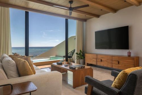 a living room with a flat screen tv and large windows at Beachfront 2BR Condo, Private Pool & Tankah Bay in Tulum