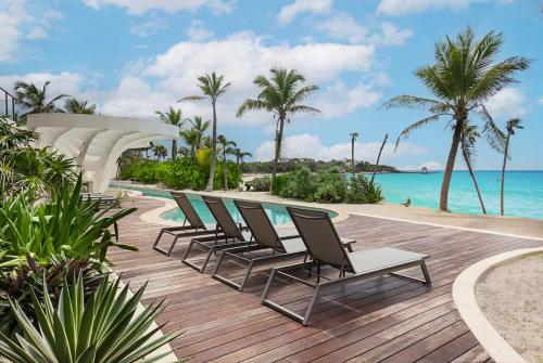 a row of chairs sitting on a wooden deck next to the ocean at Beachfront 2BR Condo, Private Pool & Tankah Bay in Tulum
