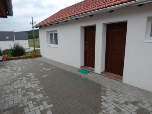 a white house with brown doors and a driveway at Tündér Szálló Eplény in Eplény