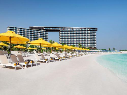 eine Reihe von Stühlen und Sonnenschirmen an einem Strand in der Unterkunft Mövenpick Resort Al Marjan Island in Ras al Khaimah