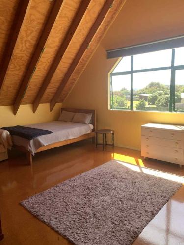 - une chambre avec un lit, une fenêtre et un tapis dans l'établissement Hosts on the Coast Titoki Palms, à Matarangi