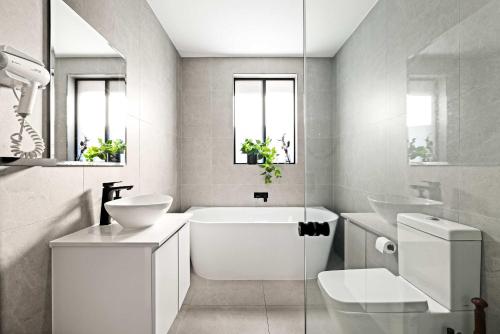 a white bathroom with a tub and a sink and a toilet at Charming Guildford Retreat - Bright Double Room Close to Green Spaces & Local Eats - Shared Bathroom in Holroyd