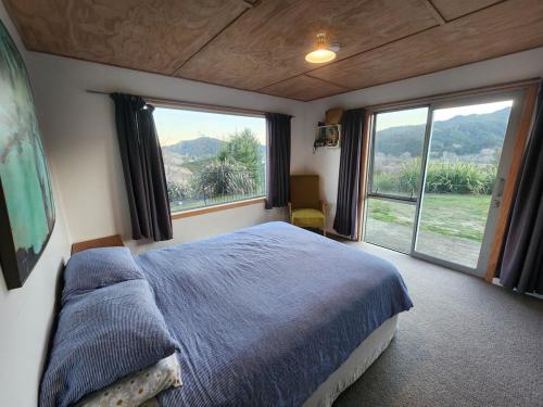 a bedroom with a large bed and large windows at Stony Ridge Summer Stay in Motueka