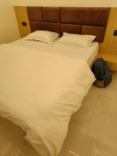 a bed with white sheets and a backpack on the floor at The Brij Retreat , 50 mtr from Shri Krishna Janambhumi in Mathura