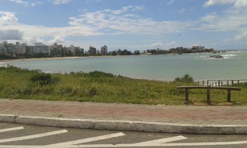 a bench sitting on the side of a beach at Pousada Enseada do Coqueiro in Guarapari