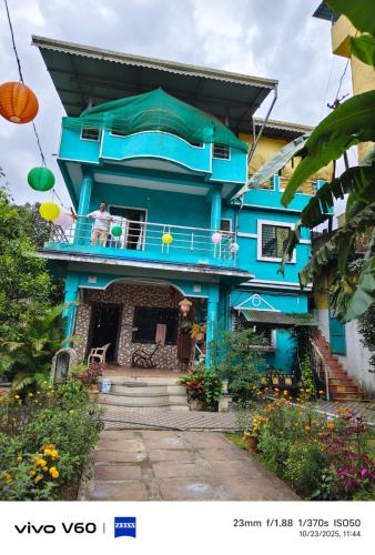 un homme debout sur le balcon d'une maison bleue dans l'établissement George Villa home Stay, à Jāmb