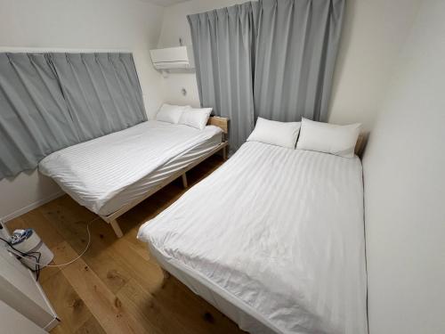 2 Betten in einem kleinen Zimmer mit weißer Bettwäsche in der Unterkunft さくら旅館 吉祥寺千利休301号室 in Musashino