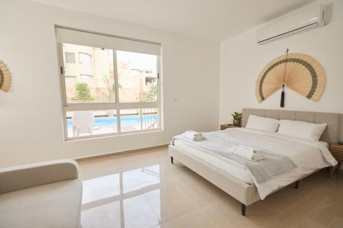 a white bedroom with a bed and a large window at אריה במדבר - וילה מושלמת עם בריכה פרטית מחוממת באילת in Eilat