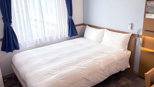 a bedroom with a white bed with a window at Toyoko Inn Hokkaido Tokachi Obihiro Ekimae in Obihiro