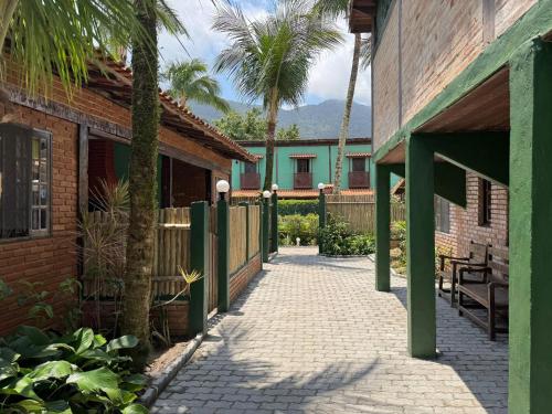 Una pasarela entre dos edificios con palmeras y una valla. en Lua Chalés 14 chalés equipados com churrasqueira individua , piscina e hidro incluindo café da manhã servido no quarto , roupa de cama, toalhas de banho e de praia a apenas 600 metros da praia de Maresias, en Maresias