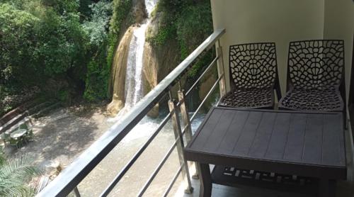 un balcon avec deux chaises et vue sur une cascade dans l'établissement Kempty Lake Waterfall Resort - Run by Anaysha Group, à Mussoorie