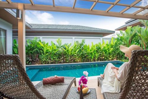 a woman sitting in a chair next to a swimming pool at Boutique 2BR Pool Villa Dalaa 1, Gated Residence, Kamala Beach in Kamala Beach