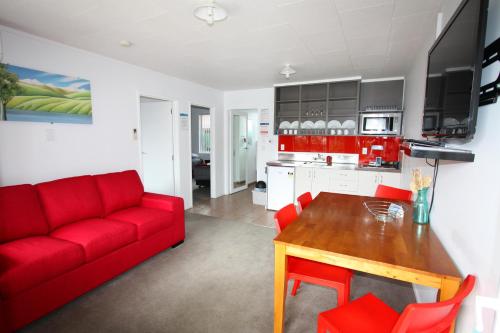 a living room with a red couch and a table at Waikanae Beach TOP 10 Holiday Park in Gisborne