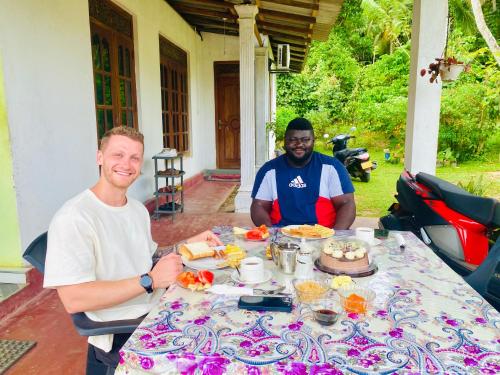 dos hombres sentados en una mesa con comida. en Hiriketiya Lima Homestay, en Dikwella