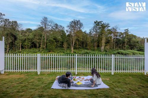 dos personas sentadas en una manta en la hierba en StayVista at Mudra Tattva - Pvt Pool,Lawn,Jacuzzi 2BR Luxury Rooms, en Suntikoppa
