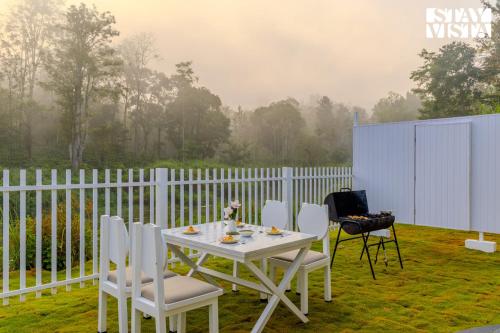 Una mesa blanca y sillas en un patio con valla. en StayVista at Mudra Tattva - Pvt Pool,Lawn,Jacuzzi 2BR Luxury Rooms, en Suntikoppa