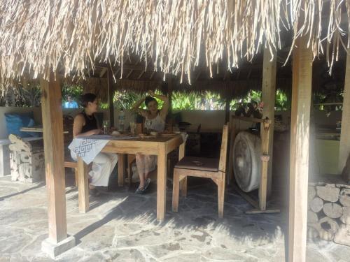 dos personas sentadas en una mesa bajo un paraguas de paja en Buku Lodge Villa Spa Lombok, en Selong Belanak
