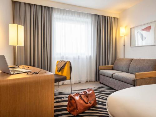 une chambre d'hôtel avec un canapé et un bureau avec un ordinateur portable dans l'établissement Novotel Marne-la-Vallée Noisy-le-Grand, à Noisy-le-Grand