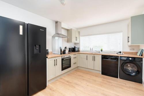 La cuisine est équipée d'un réfrigérateur noir et d'un lave-vaisselle. dans l'établissement Spacious 5 Bedroom 2 Bathroom Home with 12 Beds and Private Driveway Parking, à Manor