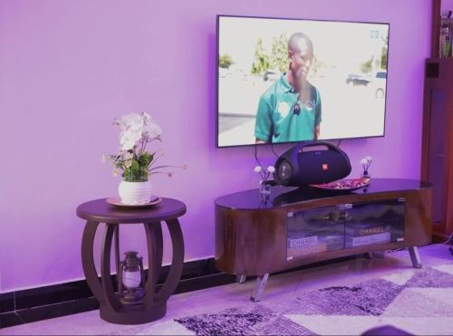 Elle comprend un salon doté d'un mur violet et d'une télévision. dans l'établissement Daud Monica Staycation Home, à Manyema