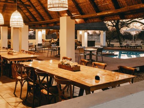 ein Restaurant mit Holztischen und -stühlen und einem Pool in der Unterkunft Tshikwalo Guest House in Klipdrift