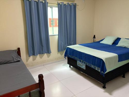 a bedroom with two beds and a window with blue curtains at Residencial Esmeralda-Vista ao Mar in Palhoça