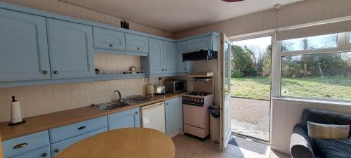 une cuisine avec des armoires bleues, une table et une fenêtre dans l'établissement Crillaun Cottage, à Foxford