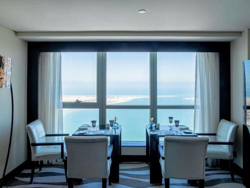 a dining room with a table and chairs and a large window at Sofitel Abu Dhabi Corniche in Abu Dhabi