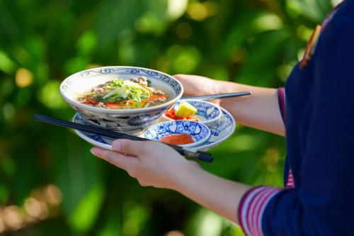 a person holding a bowl of food on a plate at Panhou Retreat in Ha Giang
