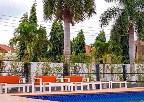 a pool with orange chairs and a fence and palm trees at Hotel Spintex and tours in Accra
