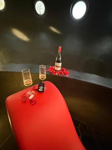 two wine glasses on a red table with a bottle of wine at tour des étoiles love room in Trévoux