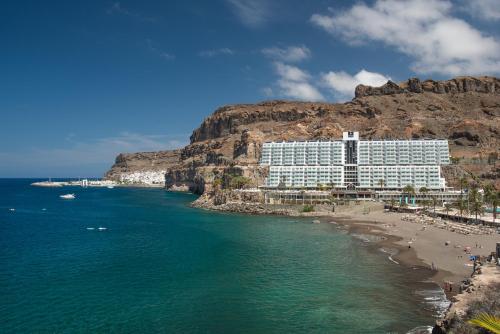 a hotel on a beach next to a mountain at Princess Taurito in Taurito
