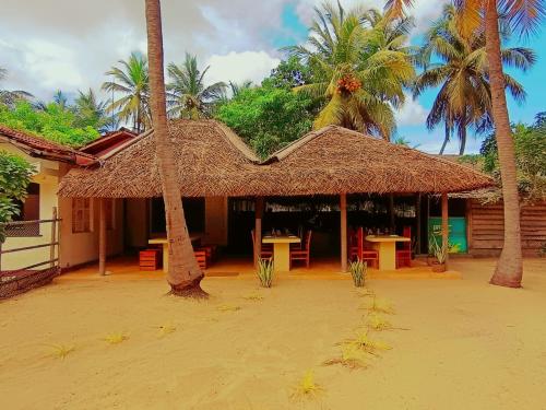 una choza de paja con mesas y palmeras en Coco Cottage Kite Surfing-Kalpitiya, en Kandakuli