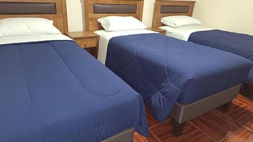three beds in a room with blue covers at Lodge Atacama Hostal in Copiapó
