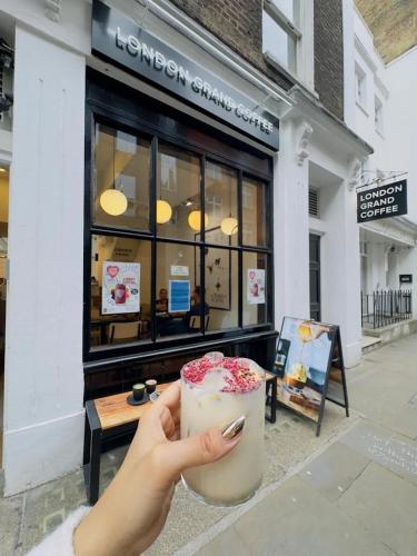 a person holding a drink in front of a store at London Grand in London