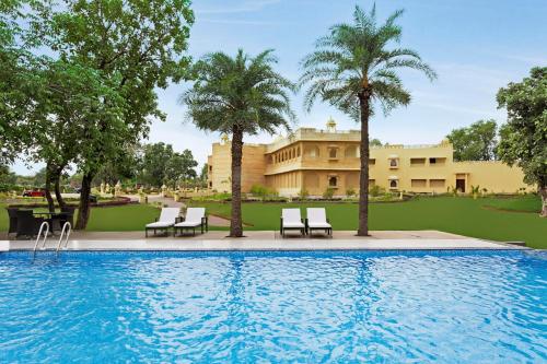 uma piscina com cadeiras e palmeiras e um edifício em Syna Heritage Hotel em Khajuraho