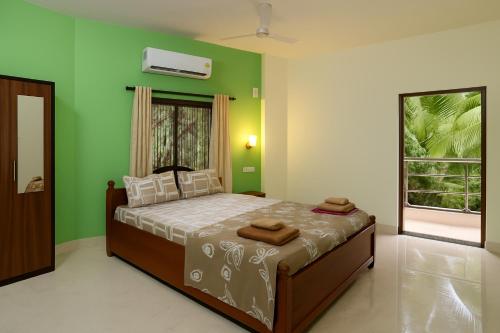 a bedroom with a bed with green walls and a window at Roque's Place Goa in Betalbatim
