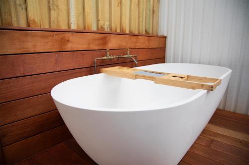 a white bath tub in a bathroom with a wooden wall at The Coconut Hut Papamoa Beach in Tauranga