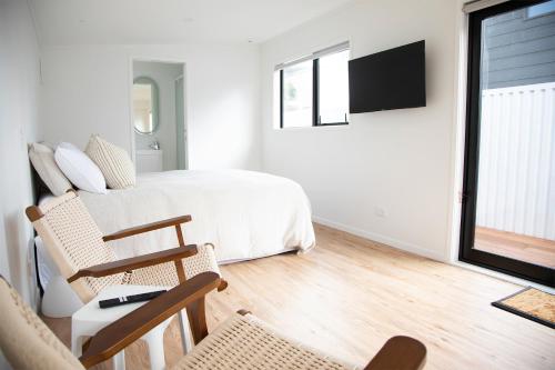 a bedroom with a bed and a tv and chairs at The Coconut Hut Papamoa Beach in Tauranga