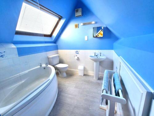 ein blaues Badezimmer mit einer Badewanne, einem WC und einem Waschbecken in der Unterkunft Shellsborough Penthouse in Woolacombe