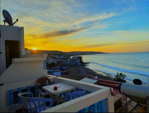 einen Sonnenuntergang vom Balkon mit einem Tisch und Stühlen in der Unterkunft Laverie du Soleil Surf House in Taghazout