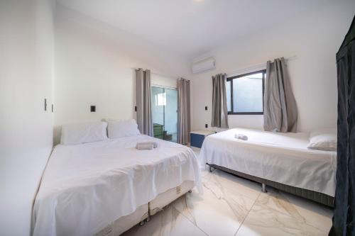 a white bedroom with two beds and a window at Casa em Bombinhas in Bombinhas