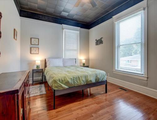 ein Schlafzimmer mit einem Bett, zwei Fenstern und einem Holzboden in der Unterkunft Modern Park Avenue Cottage in Hot Springs in Hot Springs
