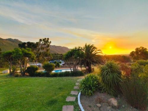 ein Sonnenuntergang über einem Park mit Pool und Palmen in der Unterkunft Into the Sunset Manor in Gordonʼs Bay