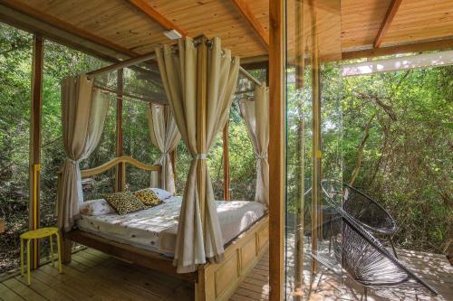 ein Bett auf der Veranda eines Baumhauses in der Unterkunft Casa de Vidro 2, há 90km de São Paulo, com Lago, Piscina, Caiaque, Stand UP, Cascata e Escorrega no Lago - Quinta do Vale Itatiba in Itatiba