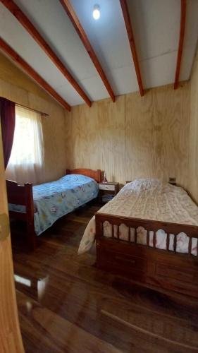 two beds in a room with wooden floors at Cabaña Pulingue-Base Camp in Ancagual