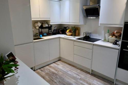 a white kitchen with white cabinets and a wooden floor at The ChurchHill in East Barnet