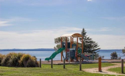 a playground with a slide in a park next to the water at Cosy cottage at Coronet Bay in Coronet Bay