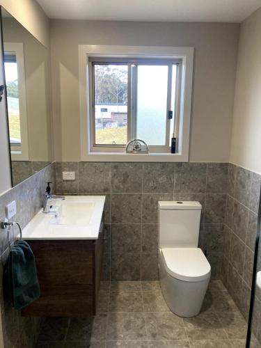 a bathroom with a toilet and a sink and a window at Jimmies on Saltwood in Tomakin